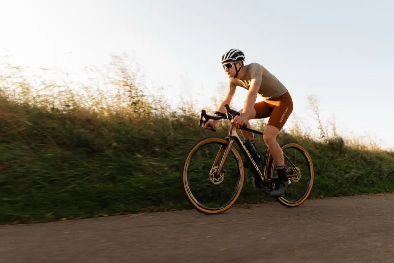 Wielrenner op een Aeross carbon fiets bij golden hour, zijprofiel dat het slanke carbon frame en de buisvormen toont